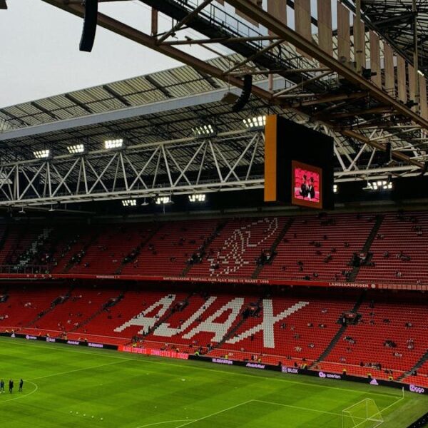 A wide view of the interior of Ajax stadium in Amsterdam, showcasing the iconic red seats and green field.