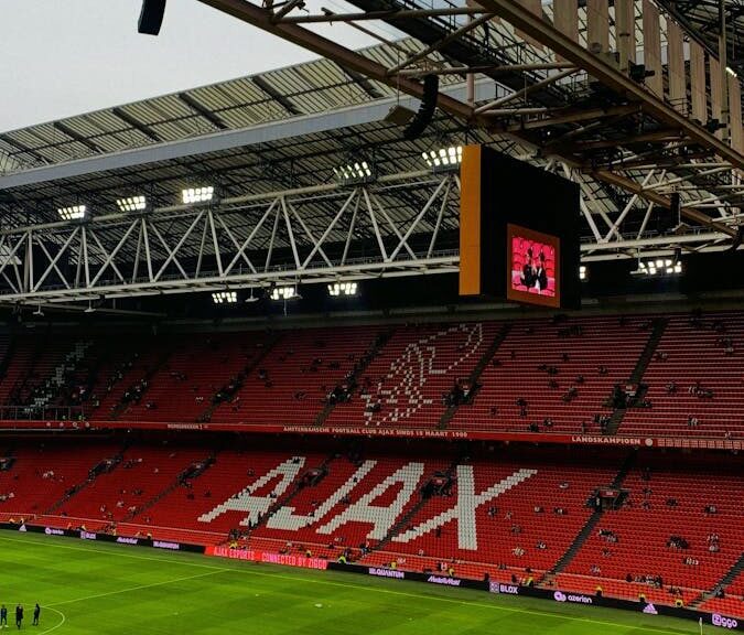 A wide view of the interior of Ajax stadium in Amsterdam, showcasing the iconic red seats and green field.