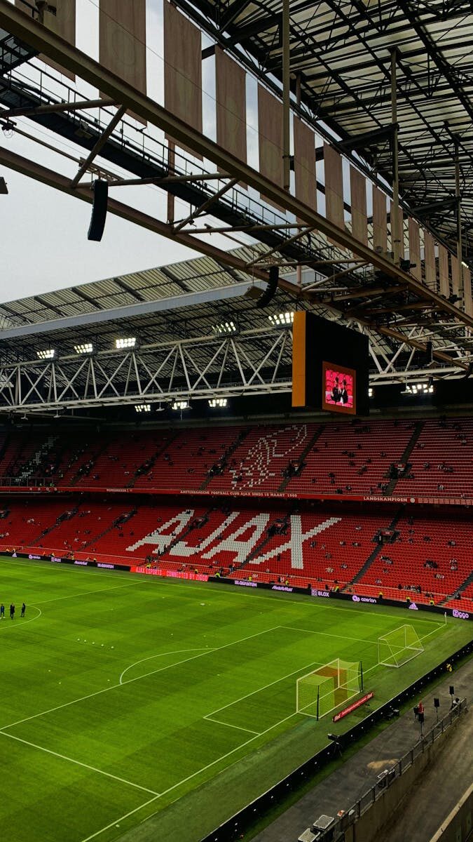 A wide view of the interior of Ajax stadium in Amsterdam, showcasing the iconic red seats and green field.