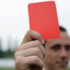 Close-up of a referee holding a red card, signaling a penalty in a soccer match.