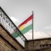 The flag of Kurdistan prominently displayed against a cloudy sky.