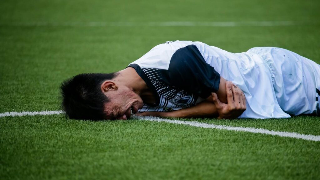 Soccer player lies on the field in pain during a game, indicating possible injury.