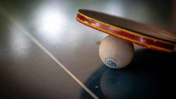 Close-up of a table tennis racket balancing on a ball indoors, emphasizing balance and sport.