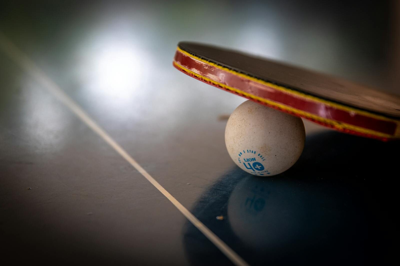 Close-up of a table tennis racket balancing on a ball indoors, emphasizing balance and sport.