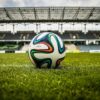 A vibrant soccer ball rests on a lush green field inside an empty stadium, capturing the essence of sports.
