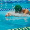 Focused swimmer in a pool during a race, featuring dynamic water splashes and vibrant turquoise water.