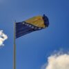 Bosnia and Herzegovina flag on a pole with a clear blue sky background in Mostar.