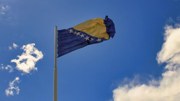 Bosnia and Herzegovina flag on a pole with a clear blue sky background in Mostar.