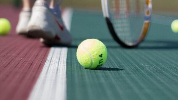A tennis ball on a court with player legs in background.