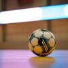 Close-up of a soccer ball on a gym floor with blurred background lights.