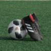 black adidas cleats lean on white and black adidas soccer ball on green grass