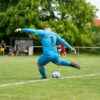 A soccer goalkeeper kicks the ball on the field.