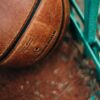 Detailed view of a leather basketball resting against a green fence on an outdoor court.