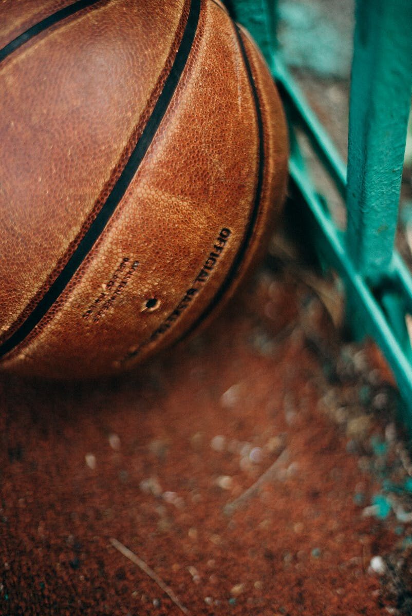 Detailed view of a leather basketball resting against a green fence on an outdoor court.