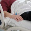 Close-up of a patient's hand with an IV drip lying on a hospital bed.