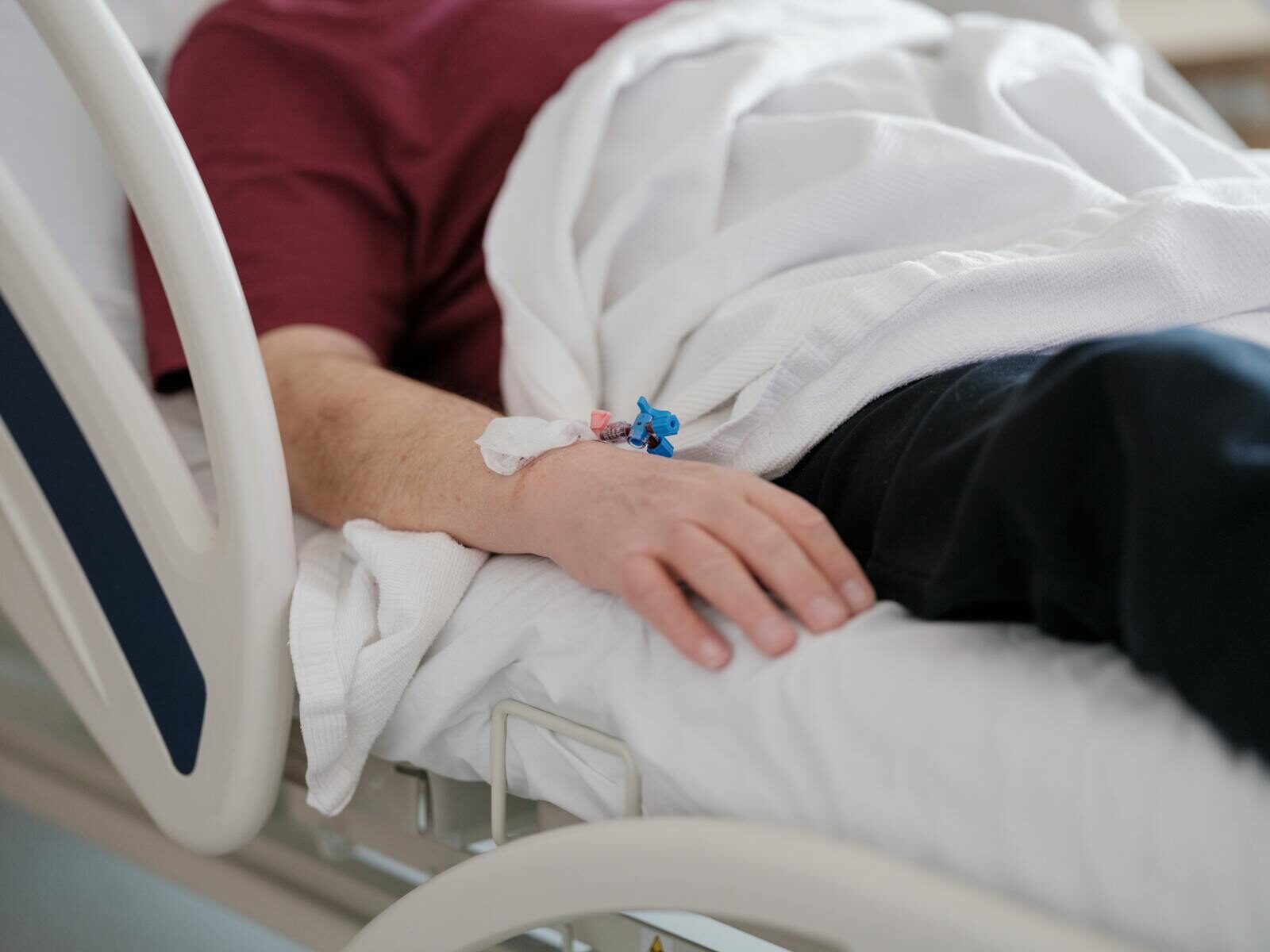 Close-up of a patient's hand with an IV drip lying on a hospital bed.