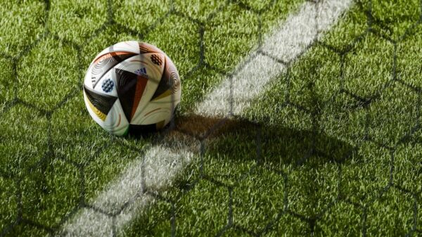 Soccer ball on a lush green field seen through netting, perfect for sports themes.