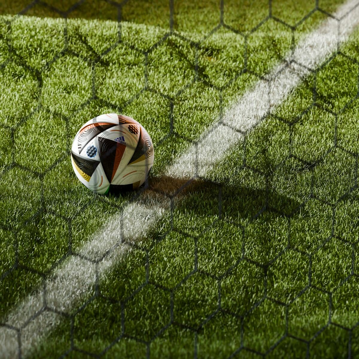 Soccer ball on a lush green field seen through netting, perfect for sports themes.