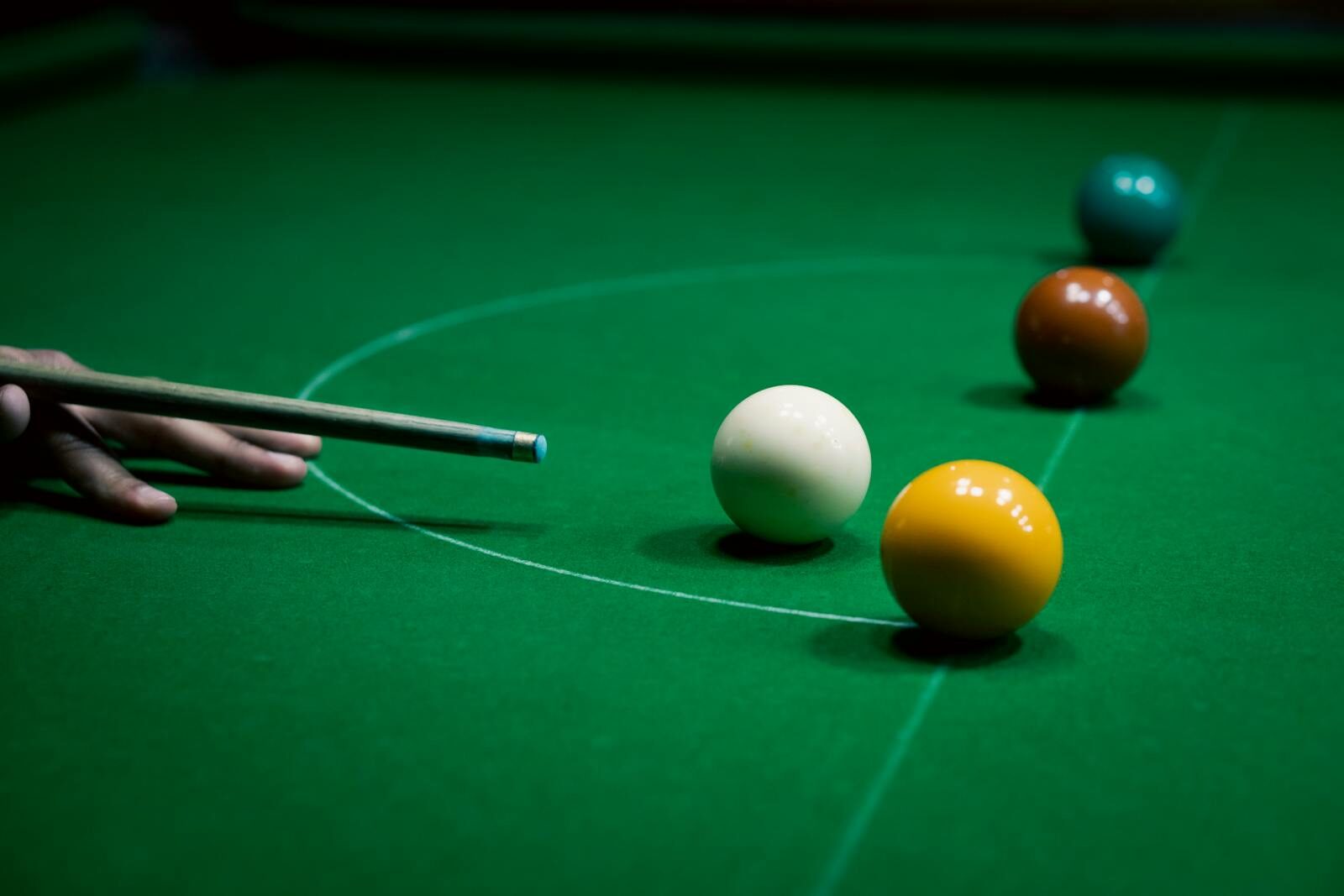 Focused shot of a snooker cue aiming at colored balls on a green table.