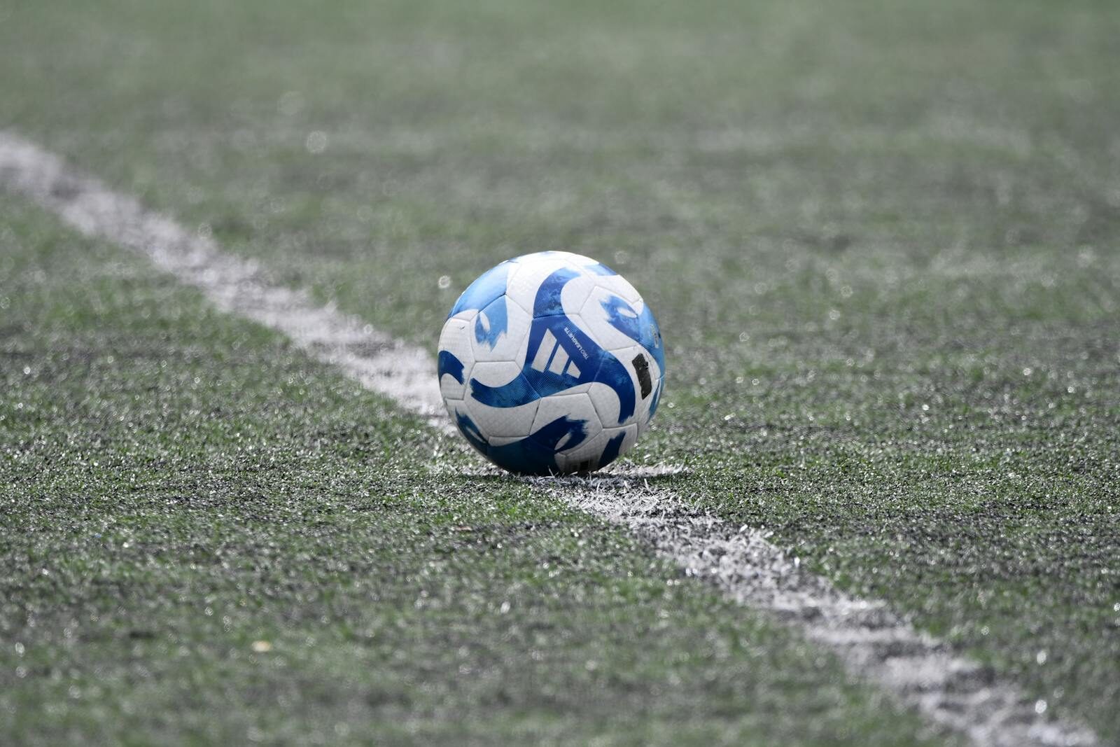 Close-up of a blue and white soccer ball resting on a lined green turf field.