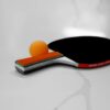 Close-up of a table tennis racket and orange ball on a white background.
