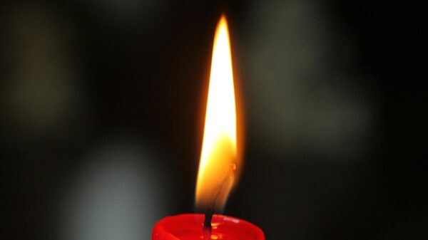 A detailed close-up of a single red candle flame glowing against a dark background, highlighting warmth and serenity.