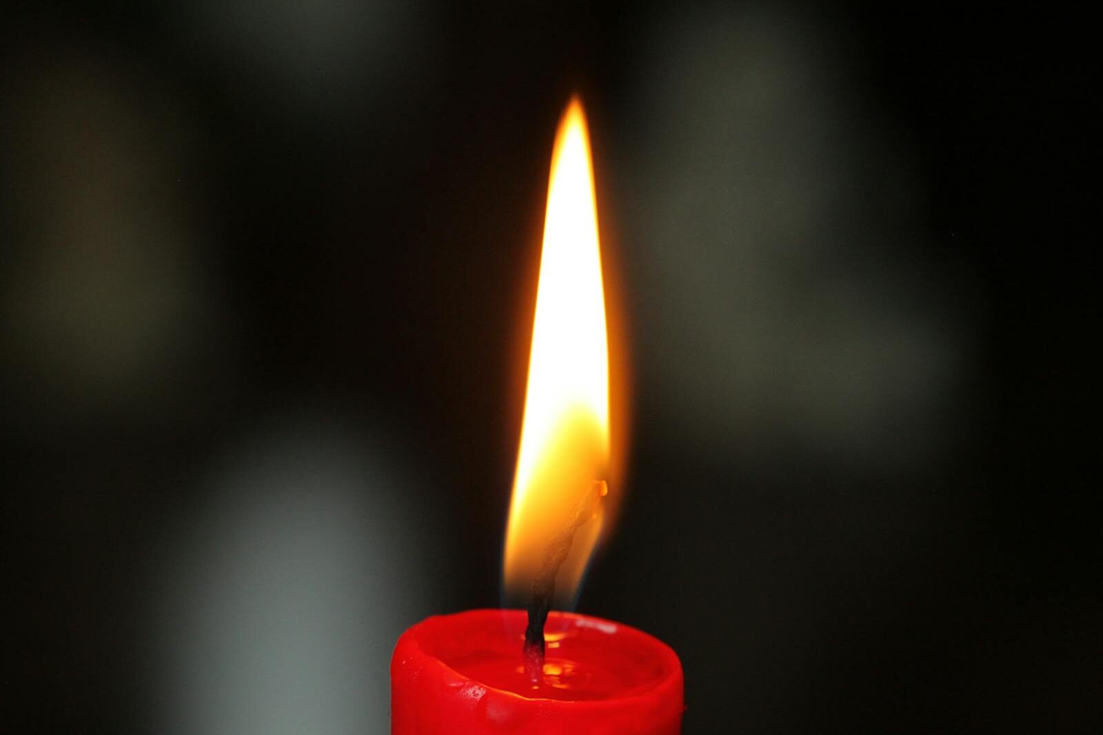 A detailed close-up of a single red candle flame glowing against a dark background, highlighting warmth and serenity.