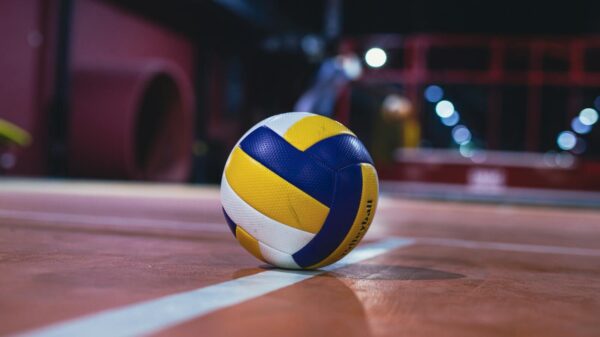 Yellow and white volleyball resting on an indoor volleyball court with bright lights.