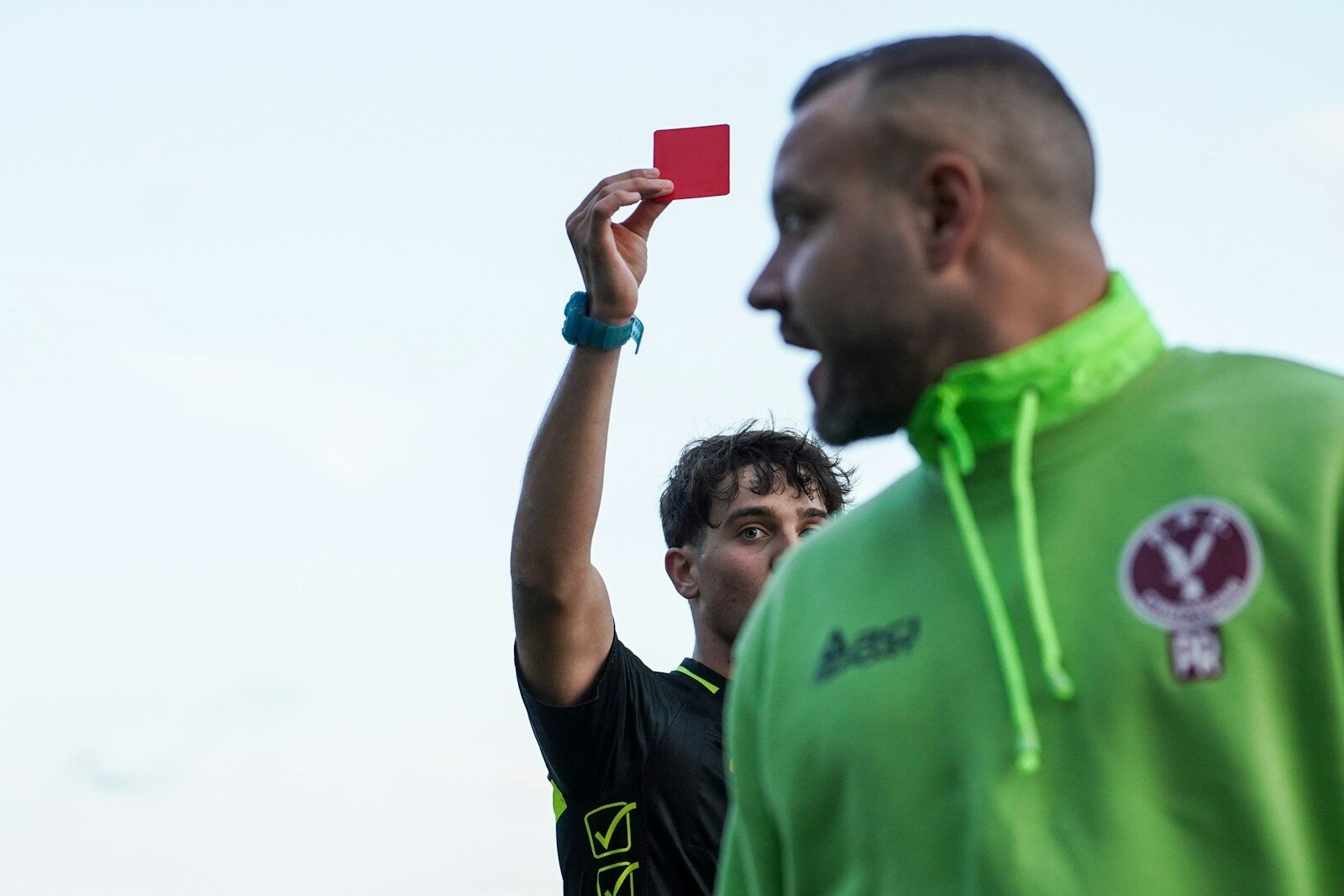 A man in a green hoodie holding up a red card