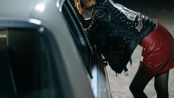 Side view of a woman in a leather jacket leaning on a car at night.