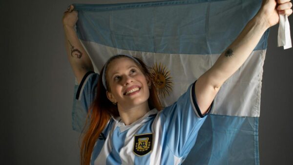 Smiling woman holding up the Argentina flag in celebration, wearing a blue and white jersey.