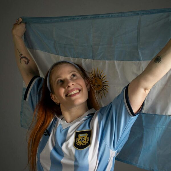 Smiling woman holding up the Argentina flag in celebration, wearing a blue and white jersey.