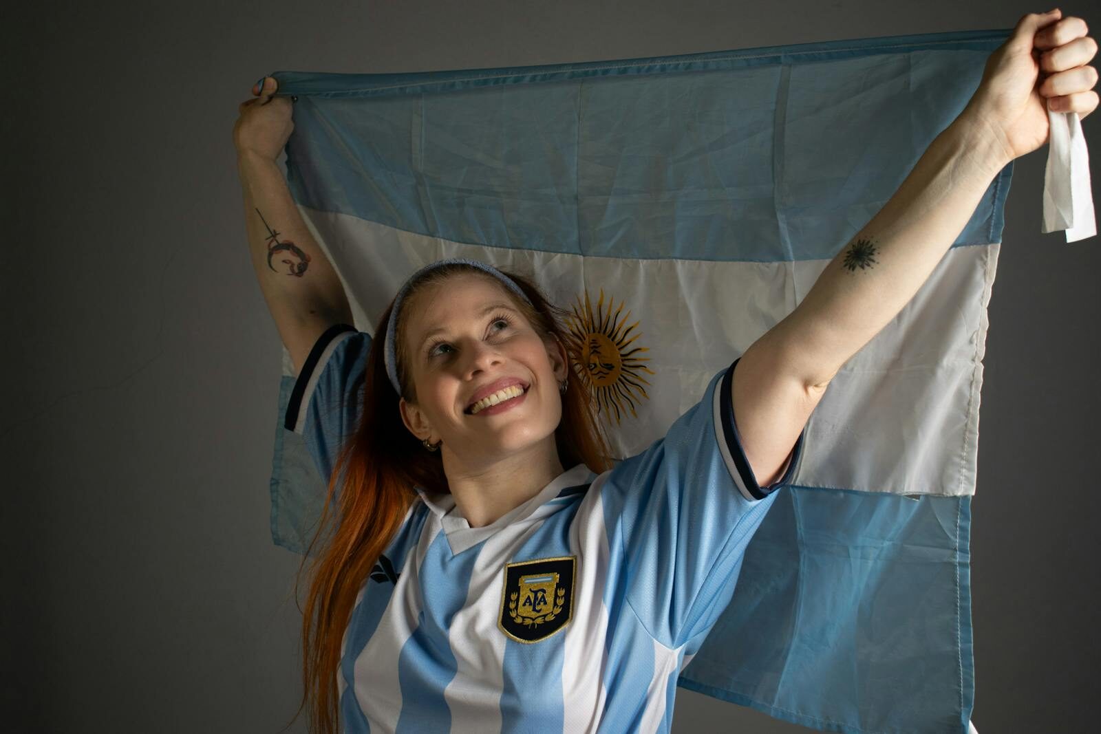 Smiling woman holding up the Argentina flag in celebration, wearing a blue and white jersey.