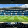 Panoramic view of Etihad Stadium, showcasing the empty football pitch and stands under a clear blue sky.