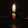 A single candle flame casting a warm glow in a dark, contemplative setting.