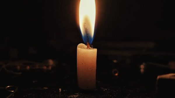 A single candle flame casting a warm glow in a dark, contemplative setting.