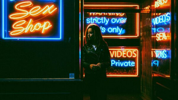 woman in black jacket standing in front of blue and red UNKs neon signage