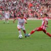 Players in action during a competitive soccer match with a vibrant crowd in the stadium.