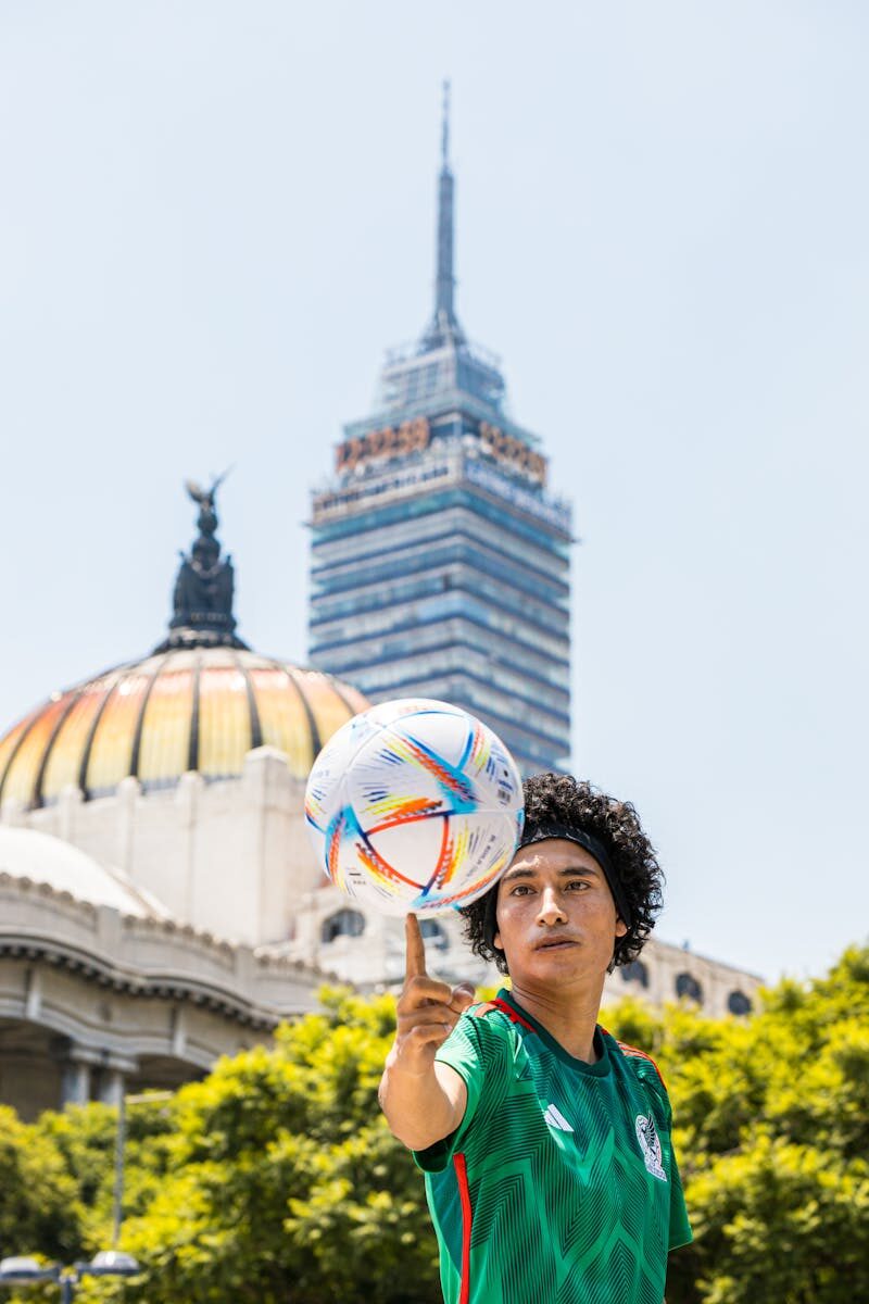 A young man spins a football in front of Torre Latinoamericana and Palacio de Bellas Artes.