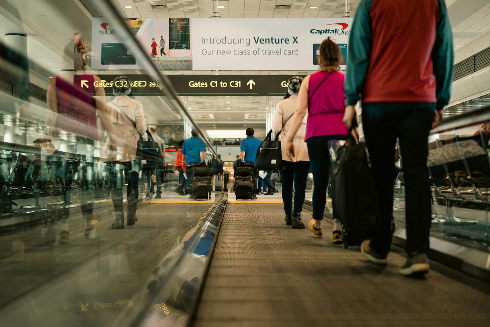 Passengers walking on a moving walkway in a busy airport terminal with signs for gates.