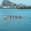 A team of rowers paddling on a serene lake in Rio de Janeiro with iconic landscape in the background.