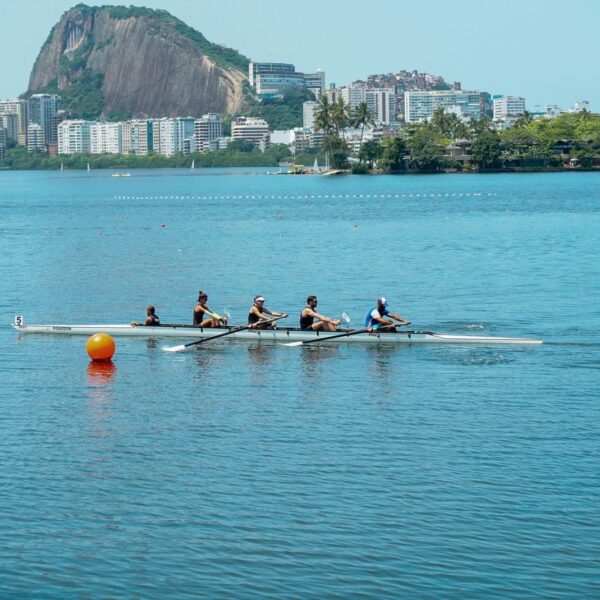 A team of rowers paddling on a serene lake in Rio de Janeiro with iconic landscape in the background.