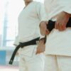 Two martial artists in white uniforms holding black belts, showcasing discipline and strength.