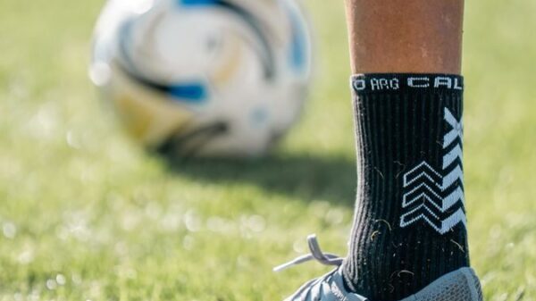 Close-up of a soccer player's foot on the field with a ball in the background.