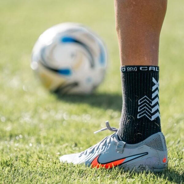 Close-up of a soccer player's foot on the field with a ball in the background.