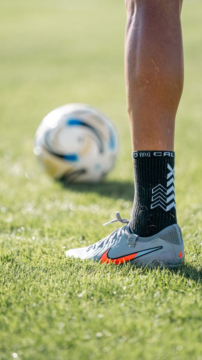 Close-up of a soccer player's foot on the field with a ball in the background.