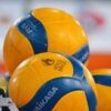 Bright yellow and blue volleyballs stacked in an indoor sports environment.
