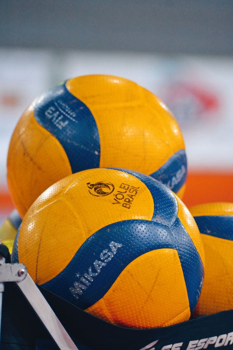 Bright yellow and blue volleyballs stacked in an indoor sports environment.