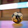 Close-up of a soccer ball on a gym floor with blurred background lights.