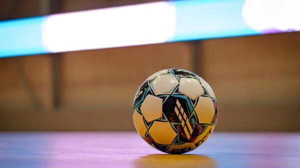 Close-up of a soccer ball on a gym floor with blurred background lights.
